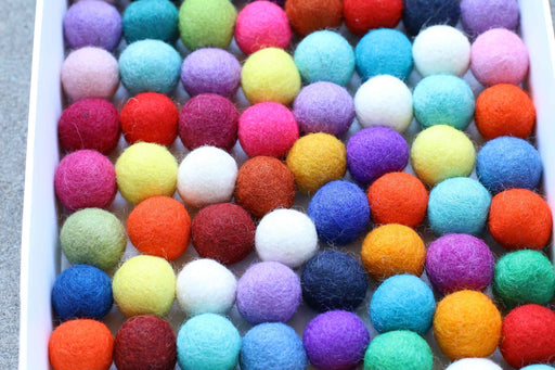A close-up view of a white tray filled with many small felt pom-poms in assorted bright colors, including pink, purple, blue, green, yellow, orange, red, and white.