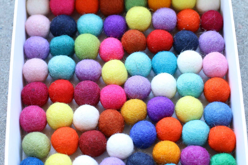 A close-up view of a white tray filled with many small felt pom-poms in assorted bright colors, including pink, blue, yellow, orange, red, purple, green, and white.