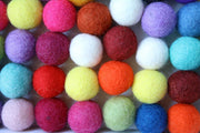 A close-up arrangement of colorful wool felt balls in multiple shades including pink, yellow, orange, blue, purple, red, white, and green.