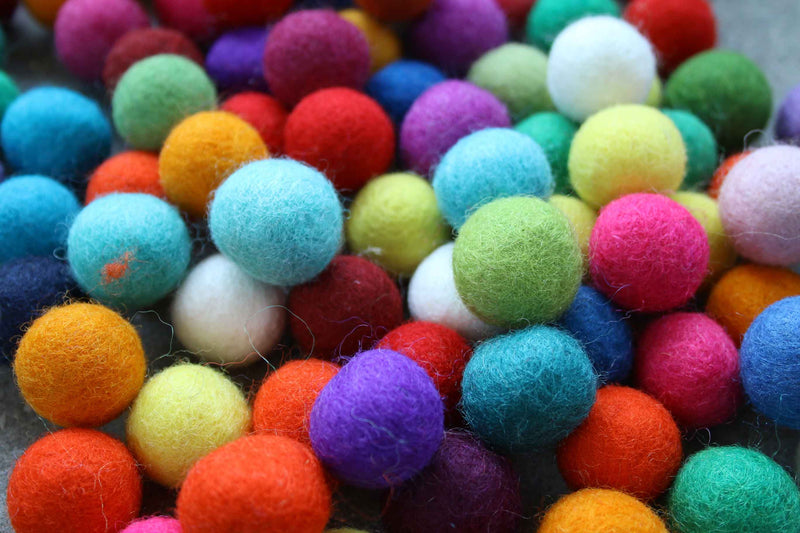 A close-up pile of colorful felt pom-poms in various shades including blue, green, pink, orange, red, purple, yellow, and white.