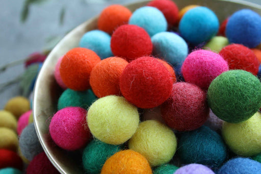 A close-up of a metal bowl filled with colorful felt balls in red, orange, blue, pink, green, yellow, and purple.